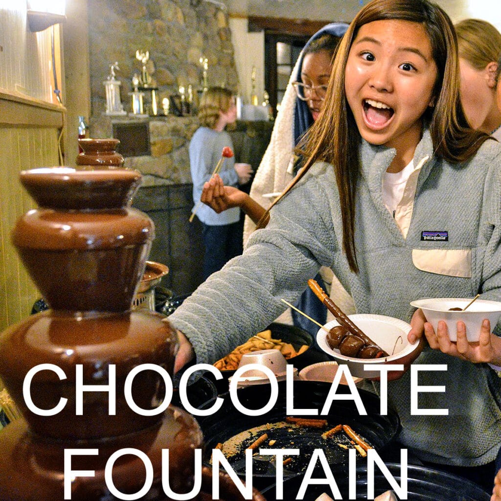 Campers dipping snacks in a chocolate fountain.