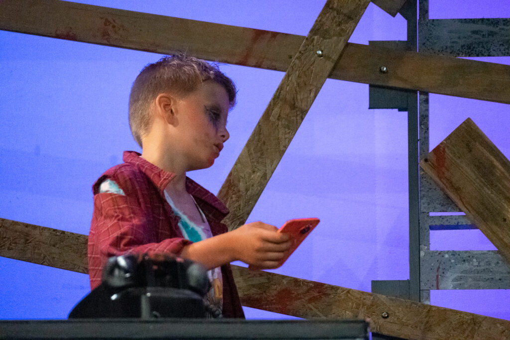 Campers performing a scene onstage with a rotary phone prop during a theater production.
