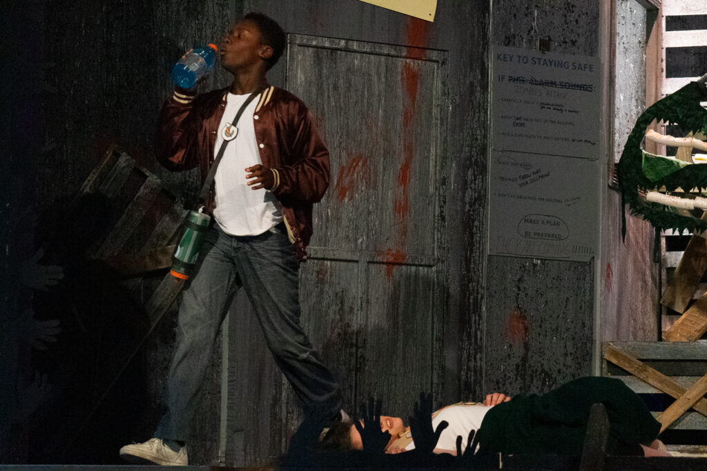 Campers acting in an intense zombie-themed stage production with dramatic set pieces.