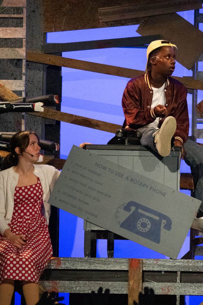 Campers performing a scene onstage with a rotary phone prop during a theater production.