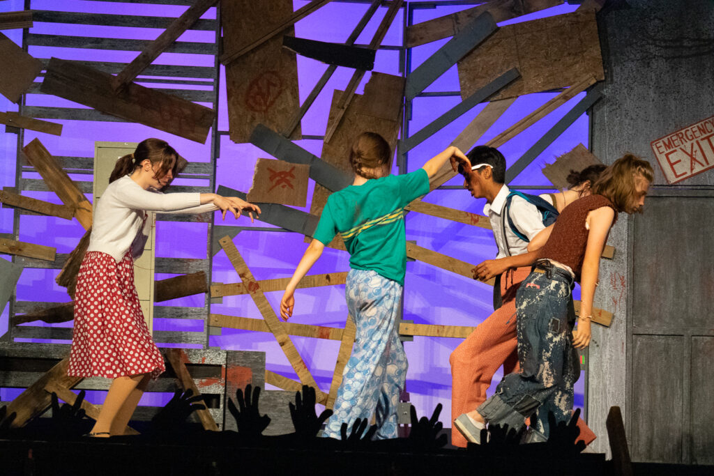 Campers acting in an intense zombie-themed stage production with dramatic set pieces.