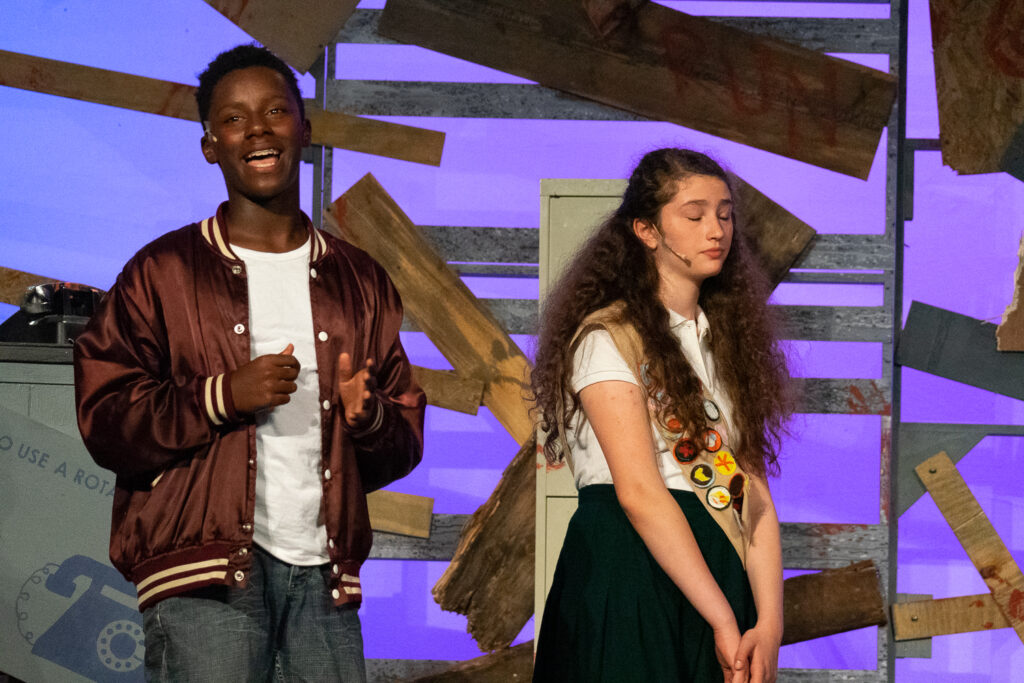 Campers performing a scene onstage with a rotary phone prop during a theater production.