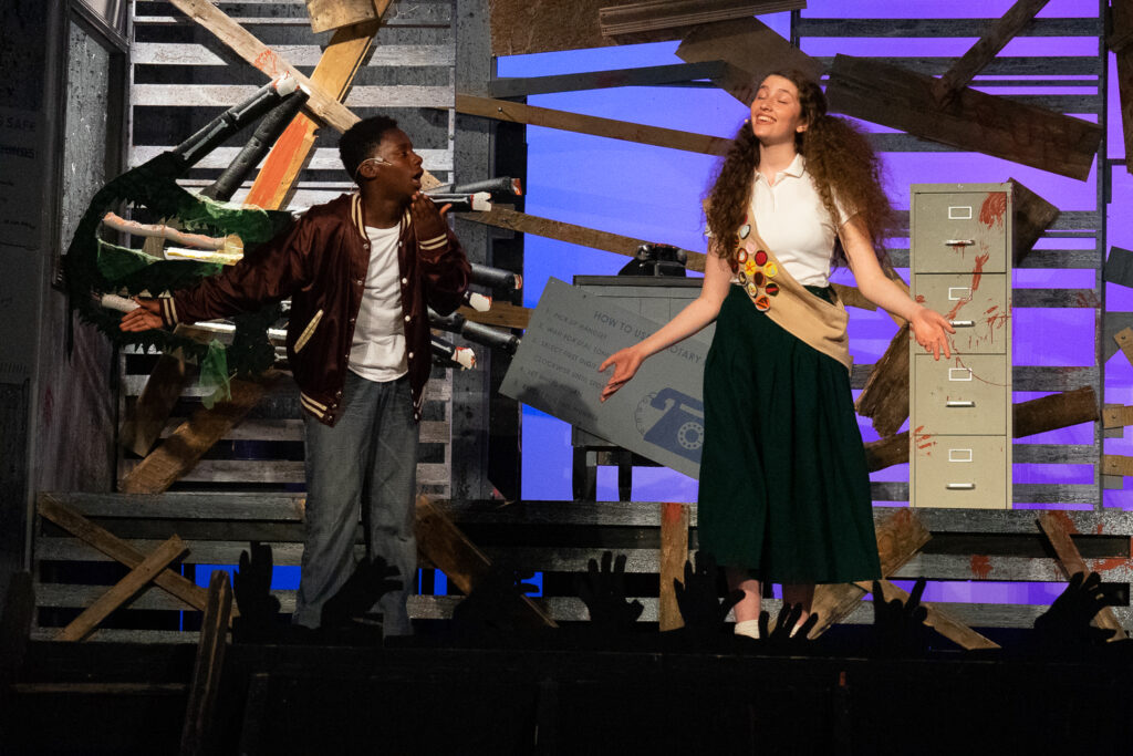 Campers performing a scene onstage with a rotary phone prop during a theater production.