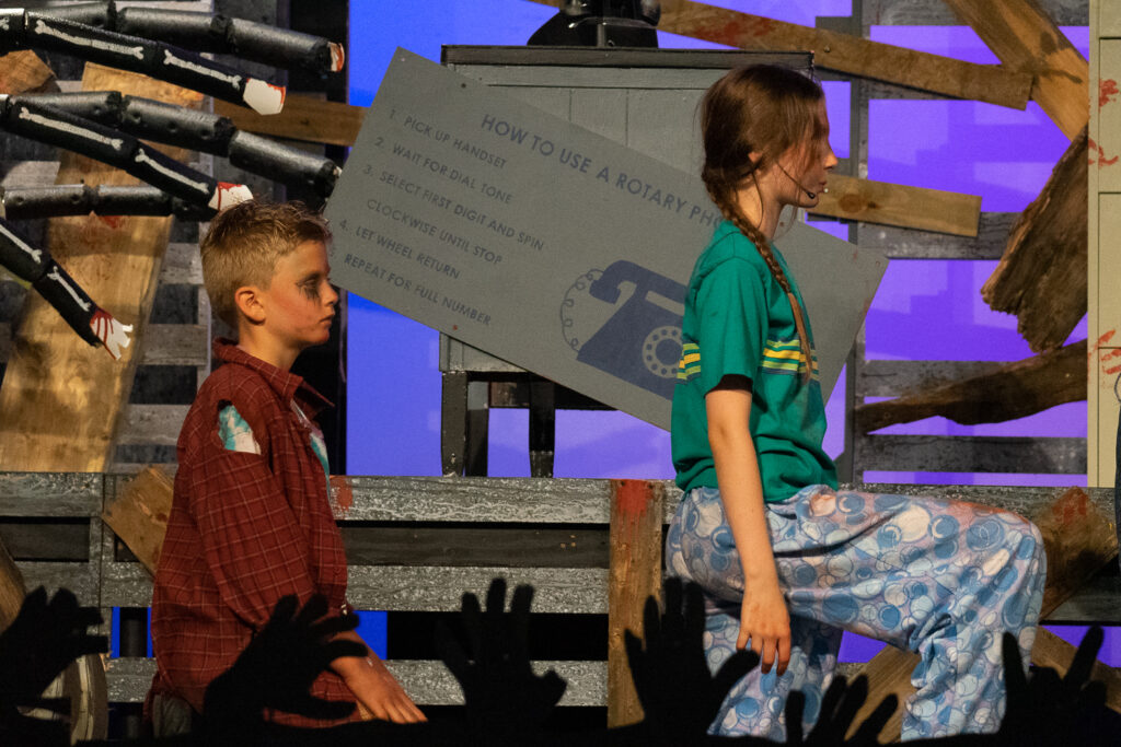 Campers performing a scene onstage with a rotary phone prop during a theater production.
