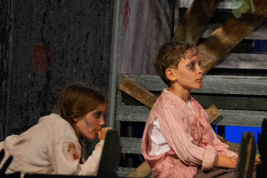 Campers acting in an intense zombie-themed stage production with dramatic set pieces.
