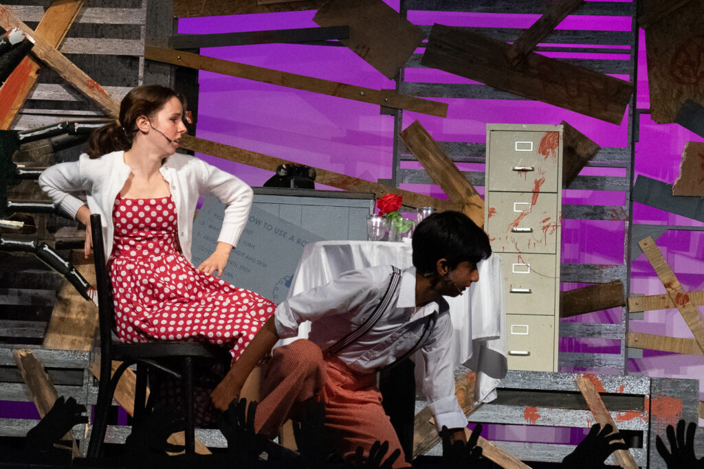 Campers performing a scene onstage with a rotary phone prop during a theater production.