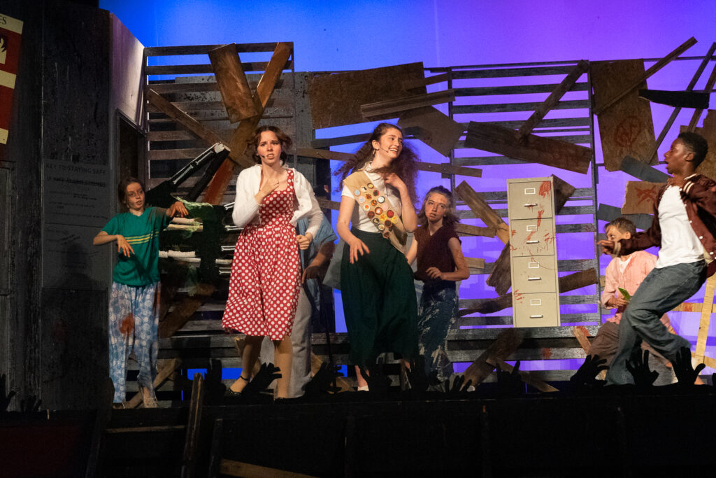 Youth actors performing a dramatic scene onstage at a summer theater camp.