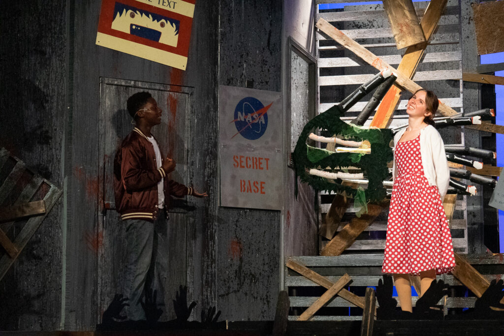 Campers acting in an intense zombie-themed stage production with dramatic set pieces.