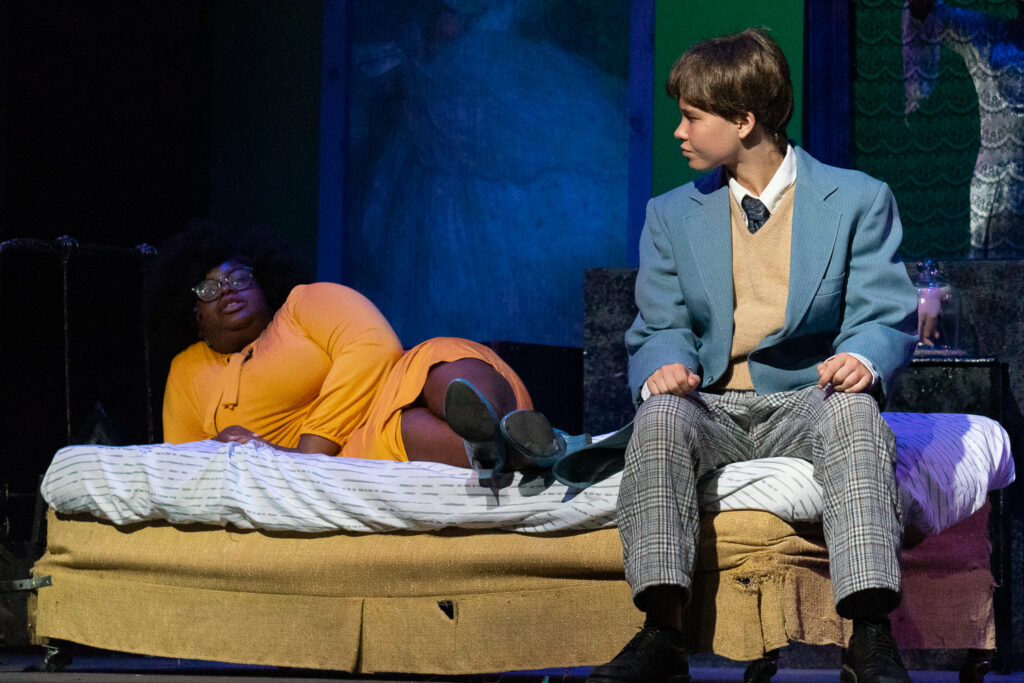 Two young actors onstage sitting on a bed during an Addams Family performance.