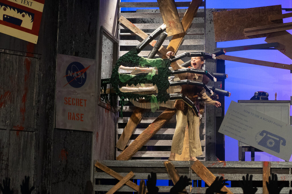 Campers performing a scene onstage with a rotary phone prop during a theater production.