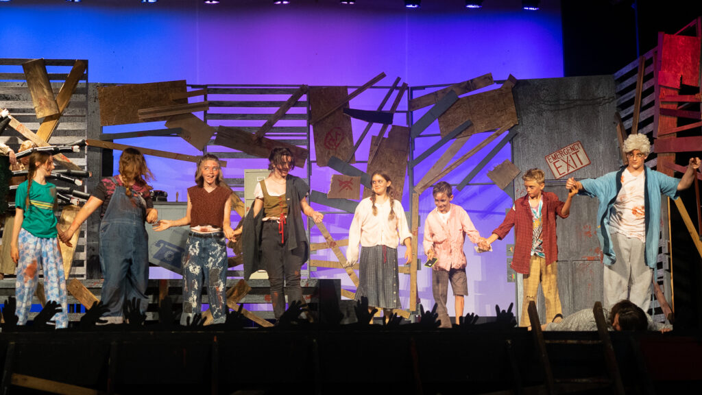 Campers acting in an intense zombie-themed stage production with dramatic set pieces.