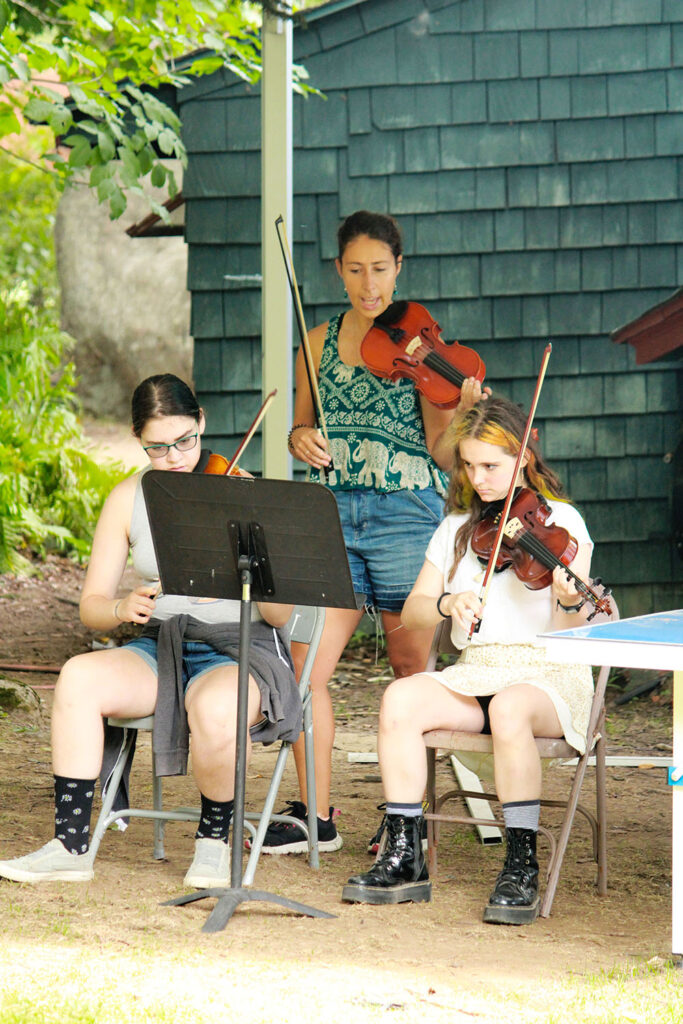 Young musicians rehearsing string instruments outdoors at Long Lake Camp