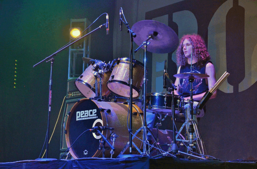 teen-boy-drum-performance-summer-camp – Long Lake Camp For The Arts A teen boy sitting confidently behind a drum set, ready to perform at a summer music camp show