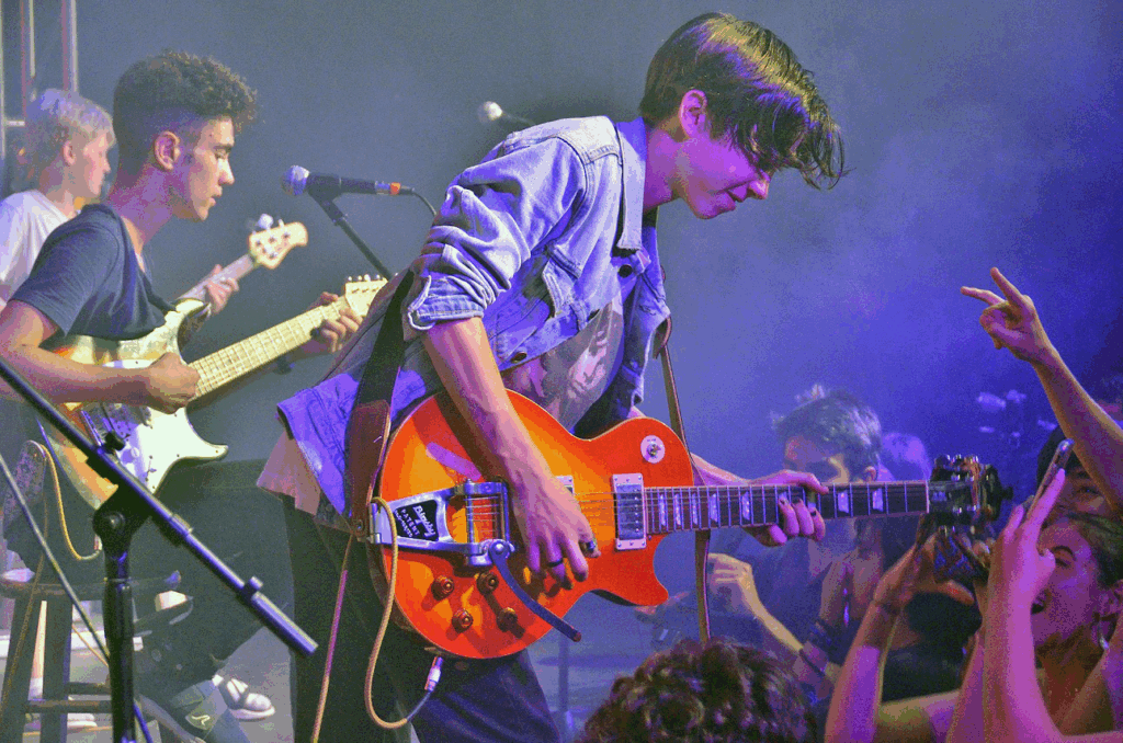 teen-boy-guitar-band-performance-summer-camp – Long Lake Camp For The Arts A teen boy singing and playing guitar alongside his band during a group performance at a sleepaway music camp