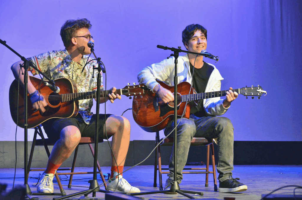 teen-boys-collaborative-guitar-performance-music-camp – Long Lake Camp For The Arts Teen boys playing guitars together on stage at a music summer camp, collaborating during a live performance