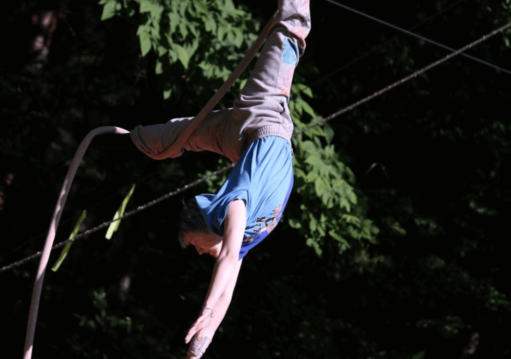 circus-arts-camp-upside-down-rope-performance – Long Lake Camp For The Arts A teen camper suspended upside down on a rope during a circus training session.