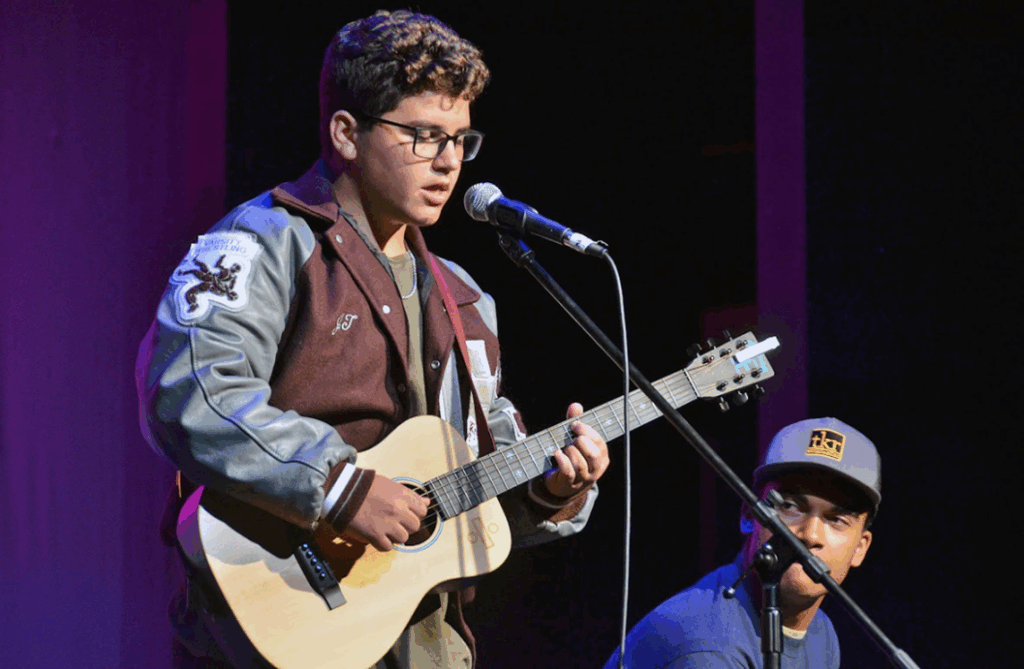 teen-playing-guitar-onstage-feedback-growth – Long Lake Camp For The Arts A teen playing guitar confidently onstage after feedback sessions at music camp