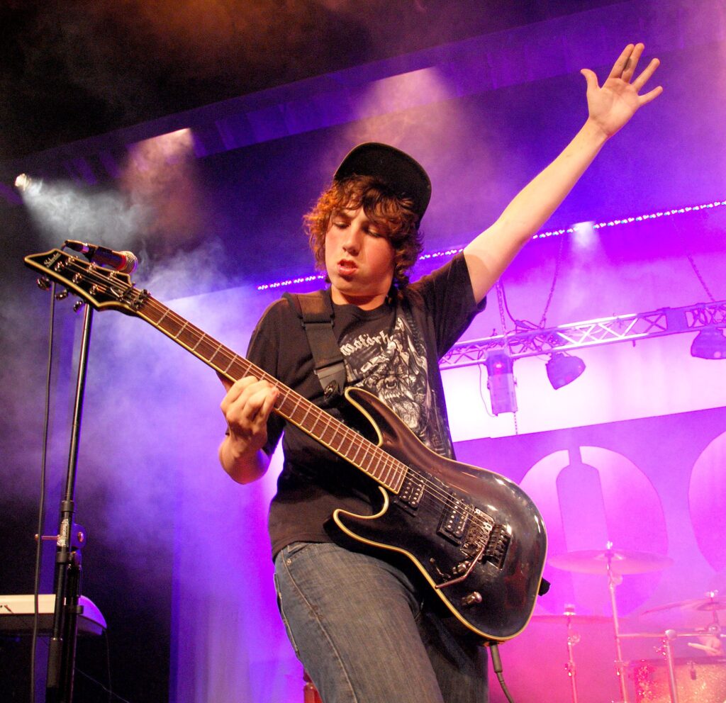 rock – Long Lake Camp For The Arts Camper playing guitar confidently on stage during Rock Night at music camp.