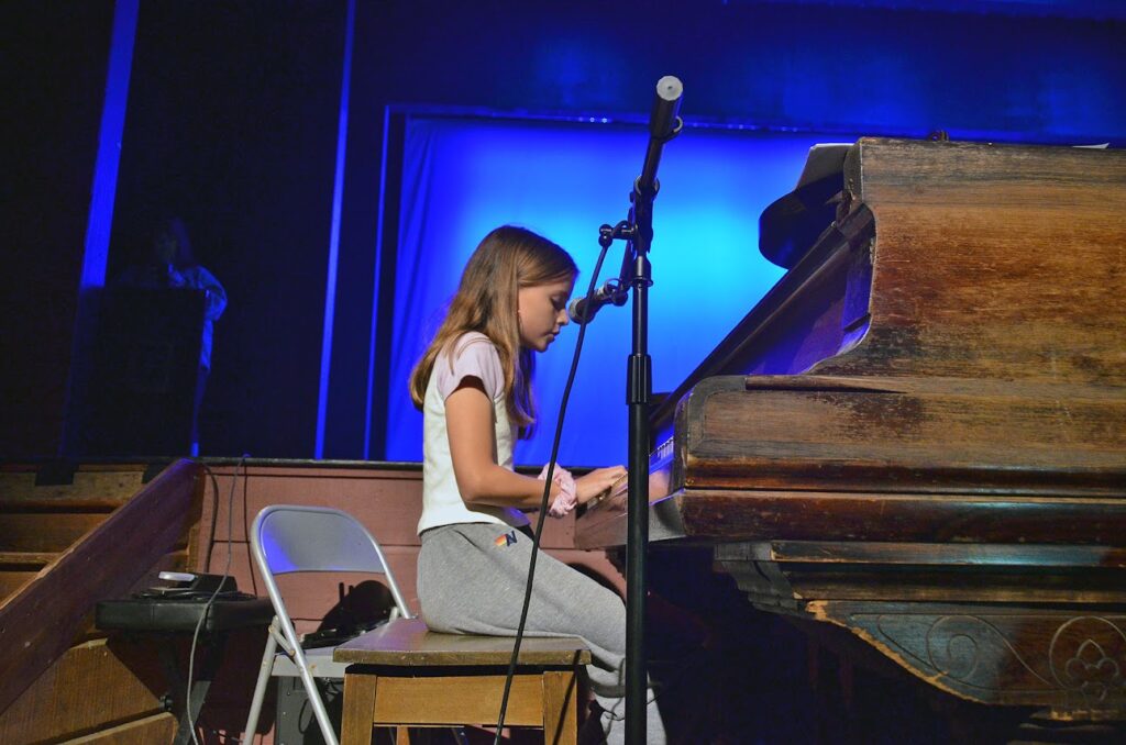 teen-camper-piano-stage – Long Lake Camp For The Arts A teen camper playing piano on stage during a music camp performance