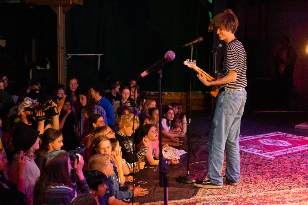 Picture20 – Long Lake Camp For The Arts A camper performing confidently on stage in front of a live audience.