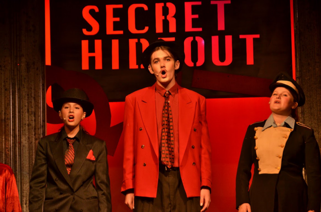Picture25 – Long Lake Camp For The Arts Campers performing a scene from Urinetown on stage