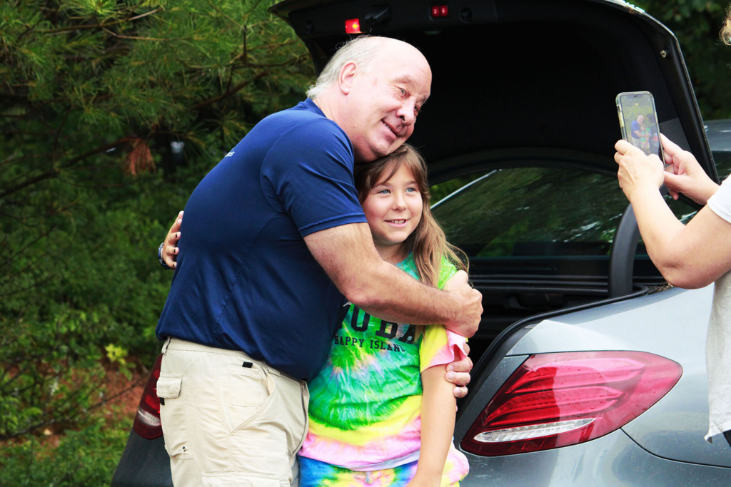A camper hugs her father while her mother captures the moment during drop-off at Long Lake Camp for the Arts.