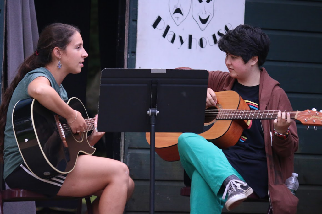 Teen campers rehearsing together and playing guitar at a summer music camp